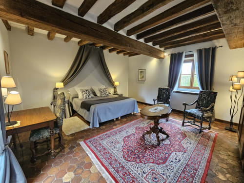 Chambre élégante aux poutres apparentes, lit à baldaquin quatre colonnes et mobilier classique du Château de Ribourdin
