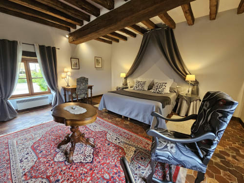 Chambre luxueuse du Château de Ribourdin avec lit à baldaquin, poutres apparentes et mobilier d'époque