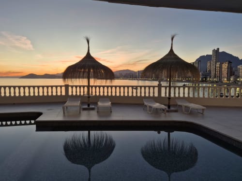 Vista al atardecer desde el balcón de Portofino Playa con sombrillas de palma, tumbonas, piscina y playa con vista a la ciudad