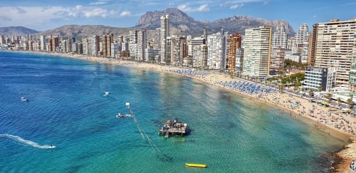 Playa de Benidorm con rascacielos, mar Mediterráneo cristalino, arena blanca con bañistas y montaña al fondo