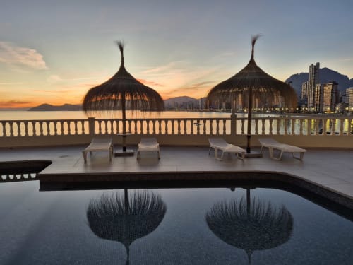 Vista del amanecer desde el balcón de Portofino Playa con sombrillas de paja, tumbonas, piscina y costa mediterránea