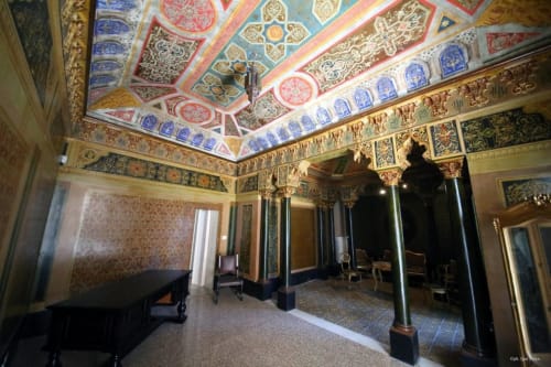 Soffitto ornato con motivi geometrici colorati nella camera Mappamondi B&B Venezia, con colonne e pianoforte