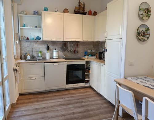 Cucina moderna nell'appartamento Casa Valentina, Ancona con mobili color crema, rivestimento scuro, pavimento in legno e tavolo da pranzo