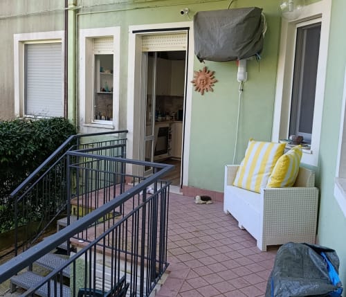 Balcone dell'appartamento di Ancona con sedute in vimini, cuscini a righe gialle e pareti verdi con vista sul giardino