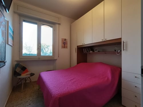 Camera luminosa con copriletto rosa, armadio integrato bianco e finestra con vista sul giardino nell'appartamento Casa Valentina, Ancona
