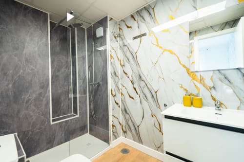Baño moderno en Los Patios De Feria Sevilla con ducha de mármol gris, lavabo blanco y paredes con azulejos veteados en oro