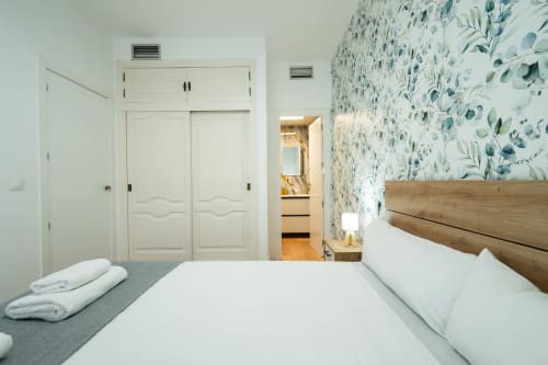 Dormitorio moderno en Los Patios De Feria, Sevilla con papel mural botánico, cama de madera y armario crema