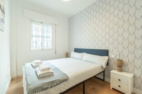 Dormitorio moderno en Los Patios De Feria, Sevilla con cama matrimonial, papel tapiz estampado, mesita de noche y ventana luminosa