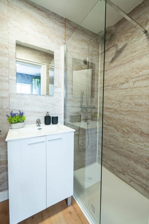 Baño moderno con baldosas efecto mármol, mueble blanco, ducha de cristal con alcachofa de lluvia en Los Patios De