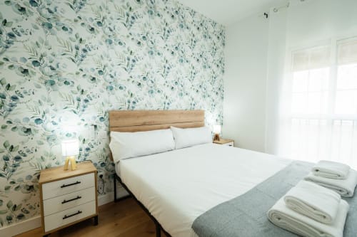 Habitación luminosa en Los Patios De Feria de Sevilla con papel pintado botánico, cama de madera, ropa de cama blanca y toallas dobladas