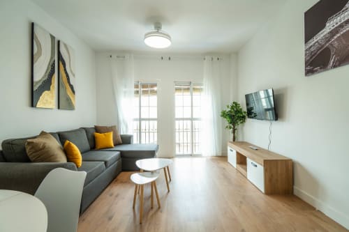 Moderna sala de estar con sofá gris, mueble de TV de madera y acceso a balcón en apartamento Los Patios De Feria, Sevilla