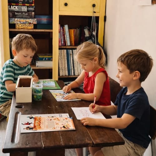 Three children engaged in creative activities at a wooden table in a vacation home at Domaine le Manoir, France.