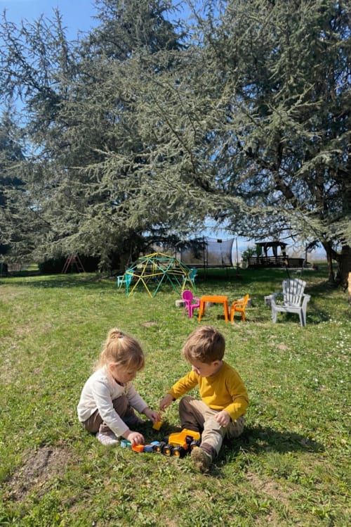 Deux jeunes enfants jouant avec des jouets sur l'herbe à Domaine le Manoir gîtes, avec équipements de jeu et cèdres