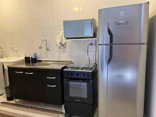 Cozinha moderna com geladeira em aço inoxidável, fogão preto, pia e TV no apartamento da Bora Bora Hospedagens, Joinville
