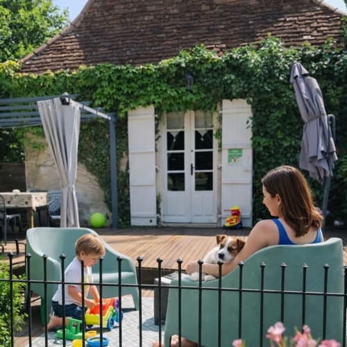 Famille profitant de la terrasse d’un gîte en Dordogne avec un enfant jouant dans le jardin
