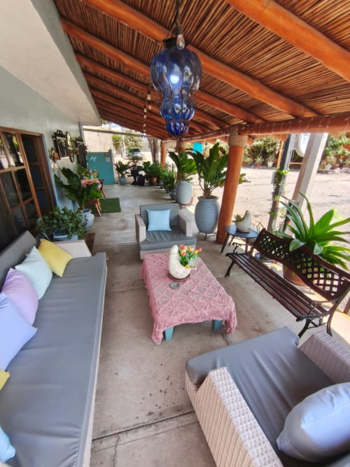 Patio cubierto con mobiliario de descanso, plantas en macetas y lámpara colgante azul en Casa Punta Perula Boutique Hotel