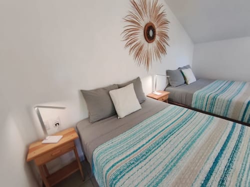 Luminosa habitación de estudio en Casa Punta Perula con dos camas, ropa de cama a rayas turquesas, mesita de noche de madera y elementos decorativos