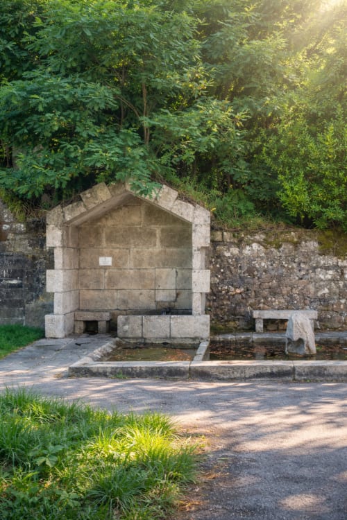 Refugio histórico de piedra con fuente y cuenca de agua rodeado de exuberante vegetación en Baiona, España