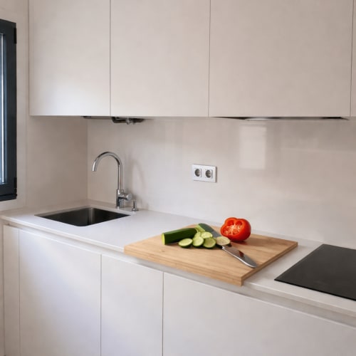 Cocina moderna con gabinetes blancos, tabla de cortar de madera con vegetales frescos, fregadero y grifo en el apartamento HoliBai