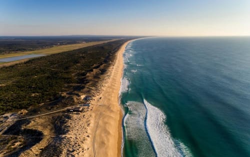 Aerial view of golden sandy beach and coastline near Canha, Portugal with turquoise ocean waves and forested landscape