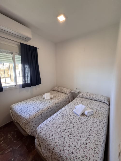 Dos camas individuales con colchas estampadas en luminoso dormitorio con vista al mar, aire acondicionado y luz de techo empotrada