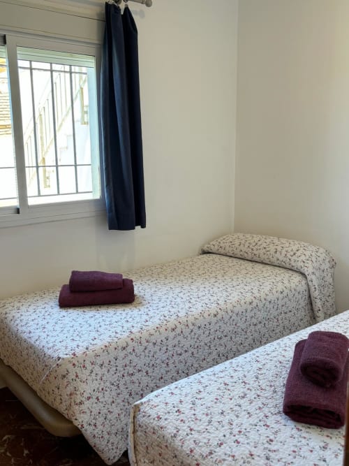 Dos camas individuales con colchas estampadas y toallas burdeos en una luminosa habitación de Apartamentos A la Orilla del Mar