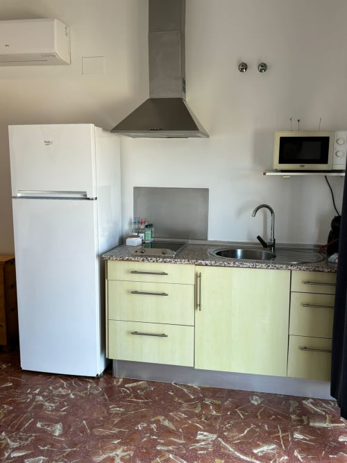 Pequeña cocina con muebles verdes, encimera de granito, refrigerador blanco y fregadero de acero inoxidable en Matalascañas