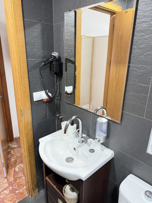 Baño moderno con doble lavamanos, paredes con azulejos negros, vanidorio de madera y espejo en Apartamentos A la Orilla del Mar