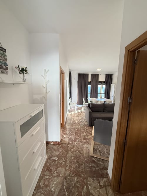 Pasillo moderno de apartamento con cocina, sala con vistas al mar, suelo de mármol marrón, gabinetes blancos y puertas de madera