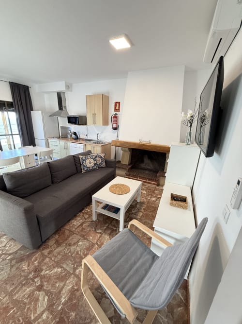 Moderno salón de apartamento con sofá oscuro, chimenea y cocina integrada en propiedad costera de Matalascañas