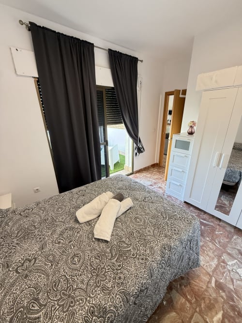 Amplio dormitorio en apartamento de Matalascañas con colcha estampada, cortinas negras, vistas al mar y acceso directo a terraza