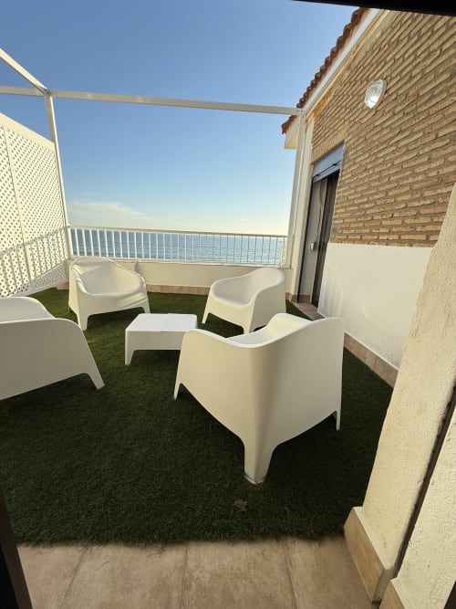 Terraza frente al mar con modernas sillas blancas y vistas al océano en Apartamentos A la Orilla del Mar, Matalascañas