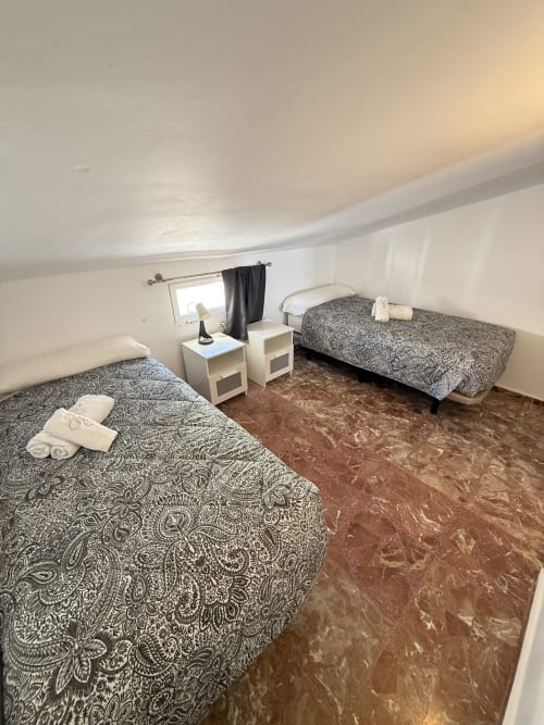 Dormitorio dúplex con dos camas, ropa de cama gris estampada, mesitas blancas y piso de cerámica marrón en Apartamentos A la Orilla
