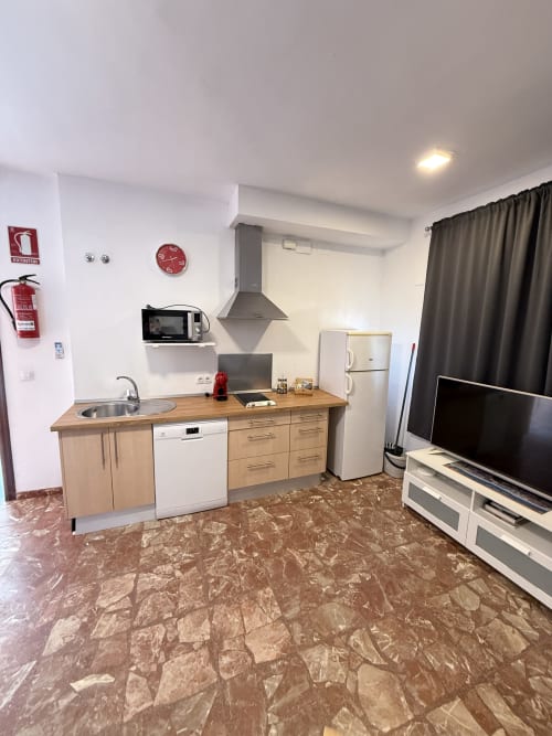 Moderna cocina con gabinetes de madera, electrodomésticos blancos y pisos de mármol en Apartamentos A la Orilla del Mar