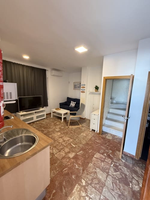 Cocina y sala de un apartamento dúplex moderno con vistas al mar, pisos de mármol, cocineta, sofá, TV y acceso por escalera