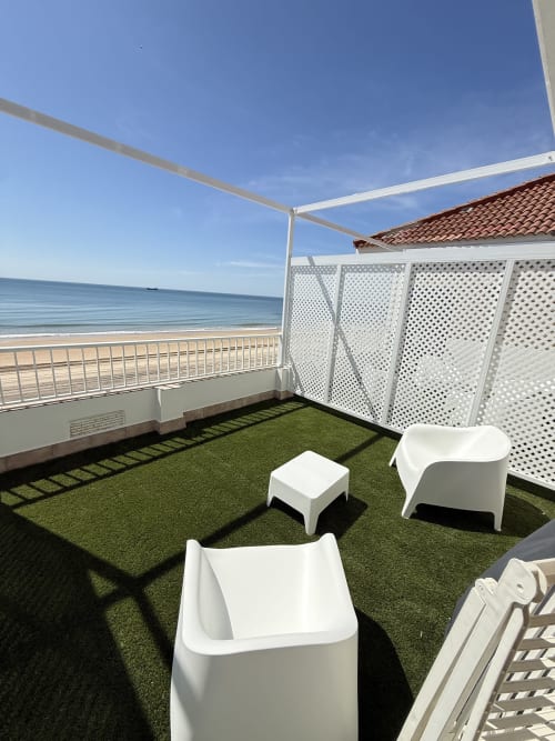 Terraza de apartamento frente al mar con césped artificial, muebles blancos y vistas al océano en Matalascañas