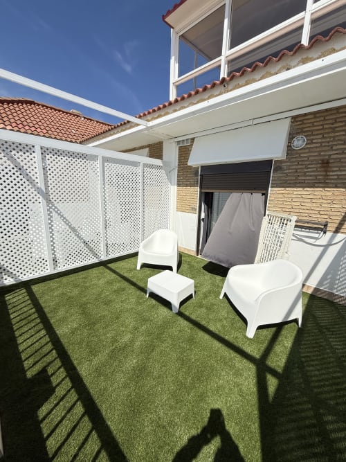 Terraza moderna con césped artificial, tumbonas blancas, biombo de privacidad y vistas al mar en Apartamentos A la Orilla del Mar