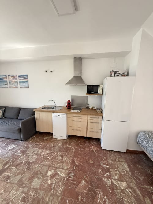 Cocina de estudio con electrodomésticos blancos, encimeras de madera y sofá gris en hotel Matalascañas