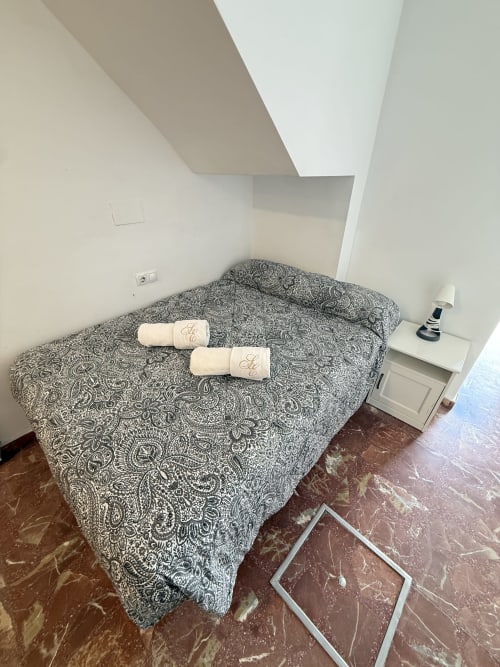 Dormitorio con colcha estampada, toallas enrolladas y piso de mármol en el Apartamento 6 de Apartamentos A la Orilla del Mar