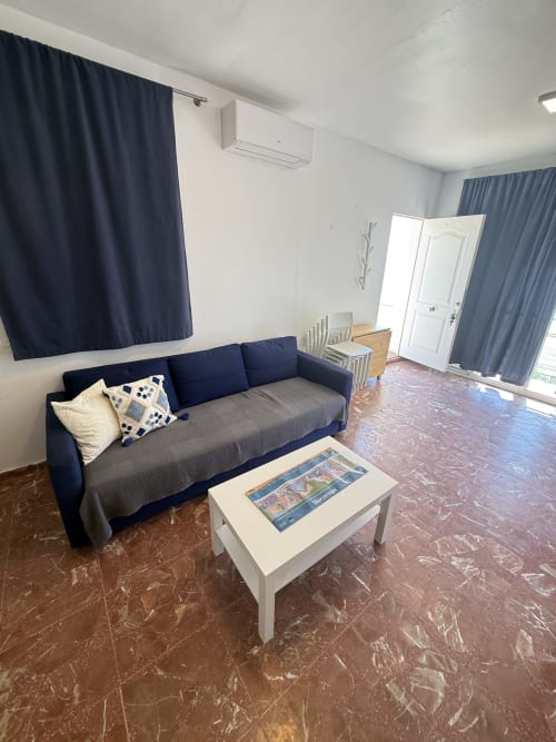 Espacioso salón de estudio con sofá azul marino, mesa de café blanca y vistas al mar en Apartamentos A la Orilla del Mar