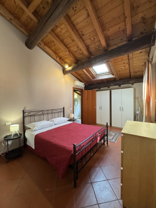 Bilocale Dalì bedroom at Corte Roveggia hotel in Verona with exposed wooden beams, wrought iron bed, and garden view