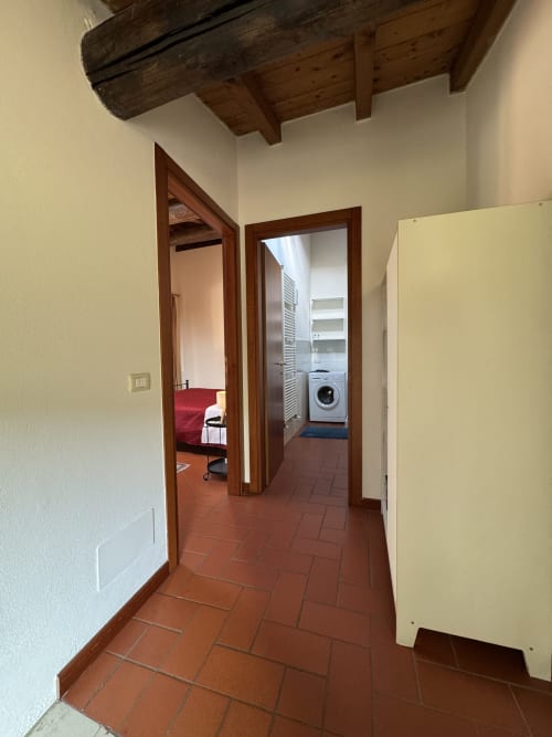 Corte Roveggia hallway with terracotta floors, wooden beams, bedroom with red bedding, and laundry room, Verona