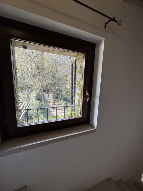 Garden view from Bilocale Dalì apartment window at Corte Roveggia, Verona, with tree-lined landscape and balcony railing