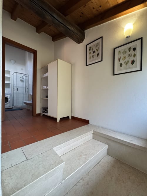 Corte Roveggia apartment entrance with marble steps, white wardrobe, botanical wall art, and bathroom access in Verona