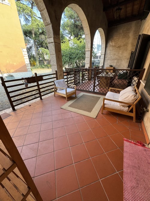 Shaded terrace at Corte Roveggia in Verona with wooden chairs, arched stonework, and garden views