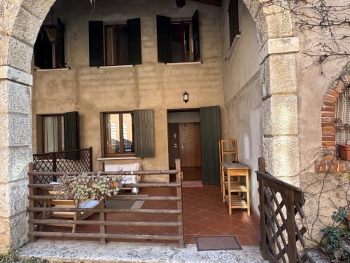 Corte Roveggia courtyard entrance in Verona with wooden seating, terracotta flooring, and green shuttered windows