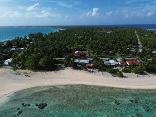 Aerial view of Tikehau Herearii beachfront bungalows with turquoise lagoon and palm trees in Tuherahera