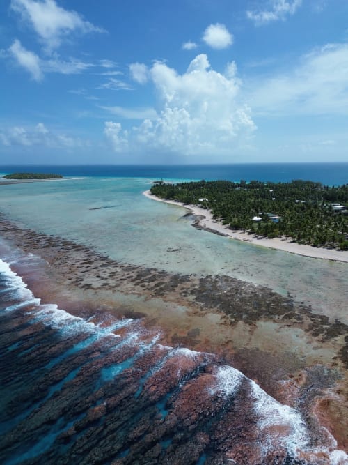 Aerial view of Tikehau atoll with turquoise lagoon, palm-lined shores, and coral reef waves in French Polynesia