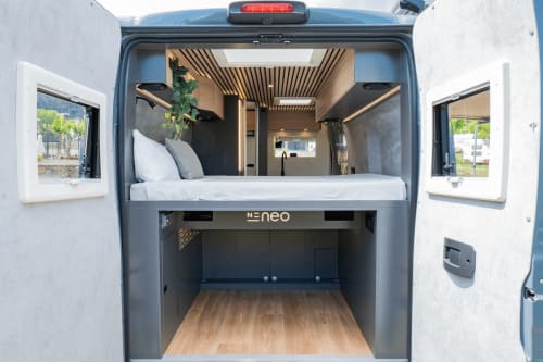 Interior de autocaravana NEO con cama queen, piso de madera, ventanas y espacio de vida compacto en hotel La Nómada