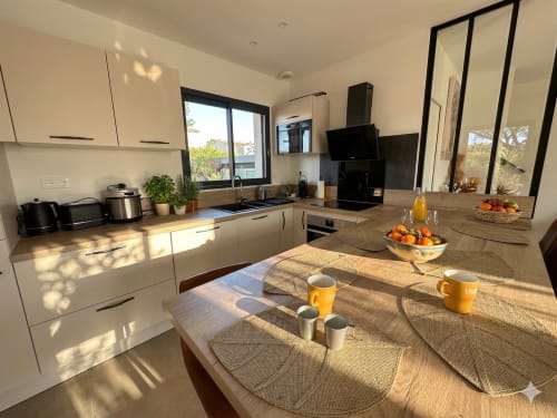 Cuisine-salle à manger moderne à La villa Métisse, Canet-en-Roussillon avec lumière naturelle, mobilier blanc et table en bois.